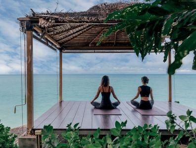 Yoga and Meditation Retreat – Seaside Yoga Session Two women practising yoga on mats overlooking the sea during a yoga and meditation retreat