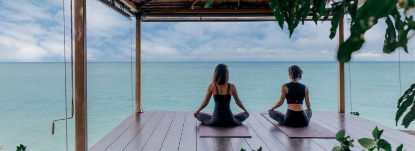 Yoga and Meditation Retreat – Seaside Yoga Session Two women practising yoga on mats overlooking the sea during a yoga and meditation retreat